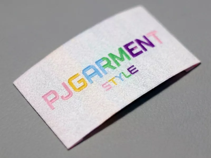 Makroaufnahme eines dicht gewebten, mehrfarbigen Halsetiketts für Nachtwäsche der Eigenmarke, das einwandfreie Fadenpräzision und luxuriöse Markenanpassung demonstriert.