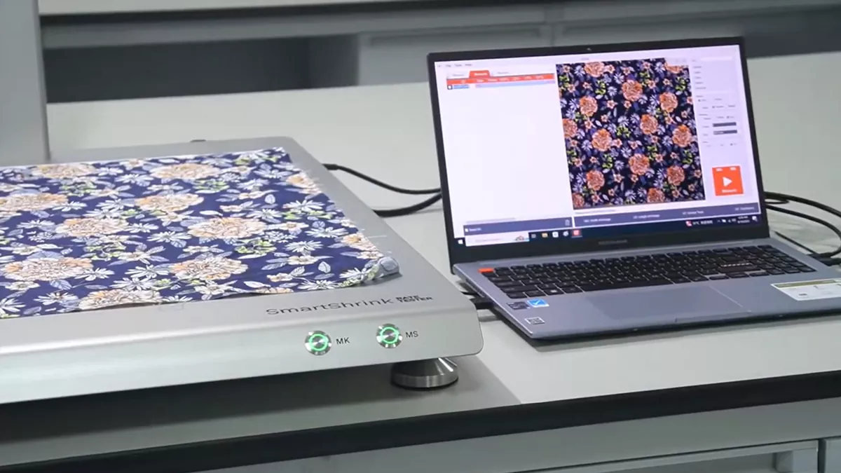 SmartShrink digital fabric shrinkage tester analyzing a floral pattern on a connected laptop, demonstrating PJGarment's precise optical quality control for warp and weft shrinkage in premium clothing sourcing.